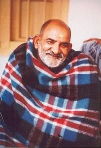 Image of Baba Neem Karori seated in a serene setting, surrounded by devotees at Kainchi Dham, Uttarakhand. The peaceful atmosphere of the temple and the lush hills in the background evoke a sense of divine presence and tranquility