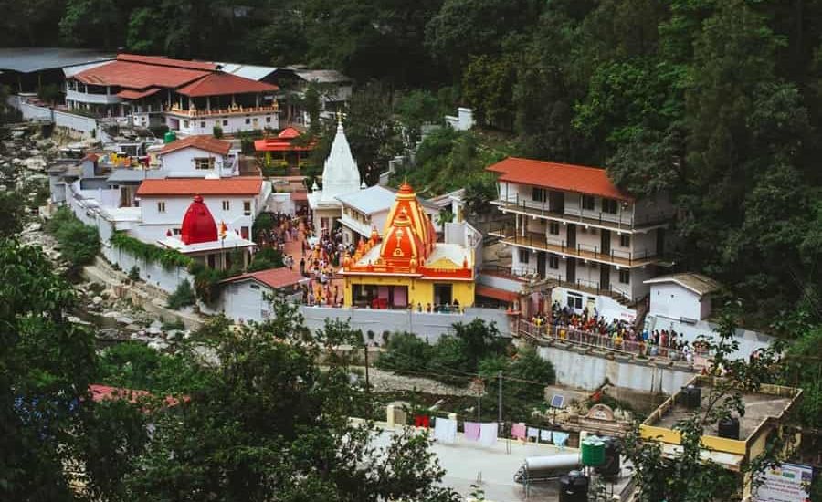 The serene Kainchi Dham temple surrounded by lush green hills, with the Kosi River flowing nearby. In the foreground, a portrait of Baba Neem Karori (Maharajji), radiating divine grace and presence, capturing the spiritual essence of the ashram
